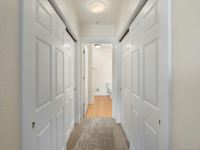 hallway featuring light colored carpet and baseboards