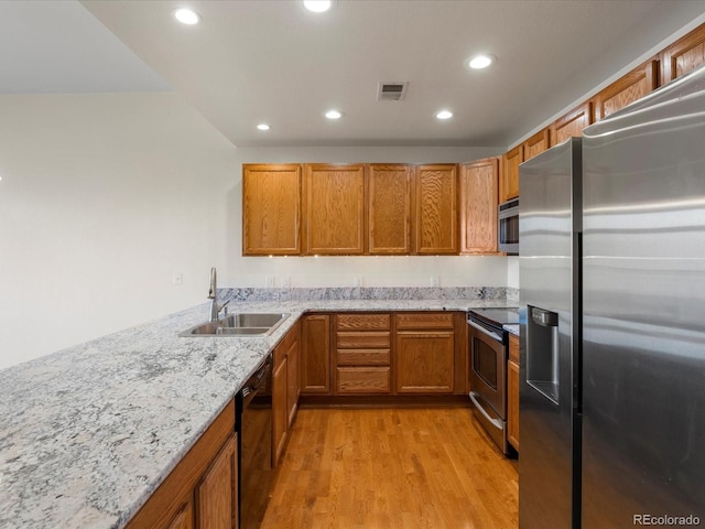 kitchen with light stone counters, appliances with stainless steel finishes, sink, and light wood-type flooring