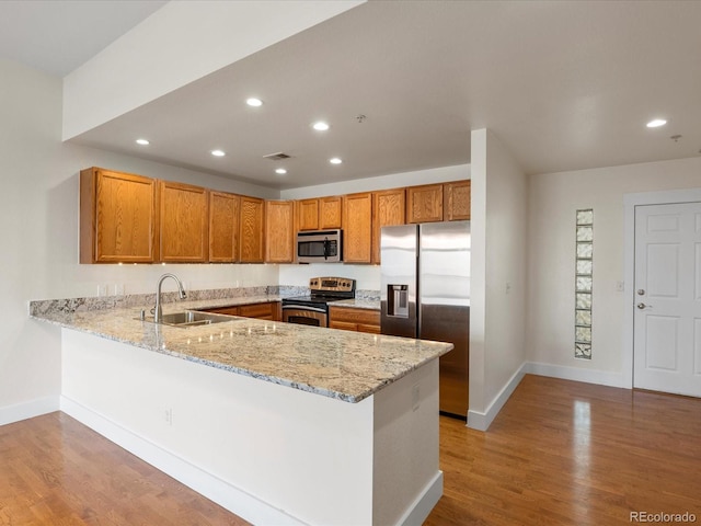 kitchen featuring a sink, appliances with stainless steel finishes, a peninsula, light wood finished floors, and light stone countertops