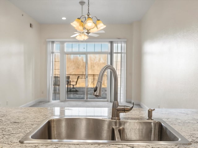 interior details featuring baseboards, pendant lighting, light stone counters, a notable chandelier, and a sink