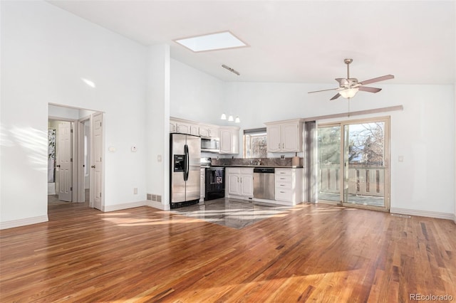 unfurnished living room with a skylight, ceiling fan, hardwood / wood-style floors, and high vaulted ceiling