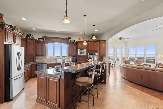 kitchen with pendant lighting, a breakfast bar area, ceiling fan, a kitchen island, and stainless steel appliances