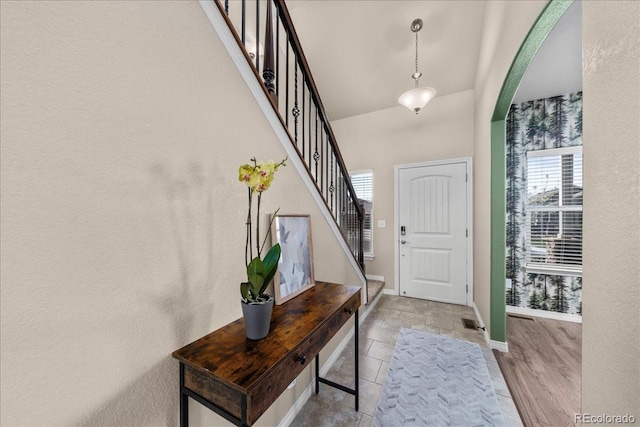 foyer with baseboards, arched walkways, stairs, and a wealth of natural light