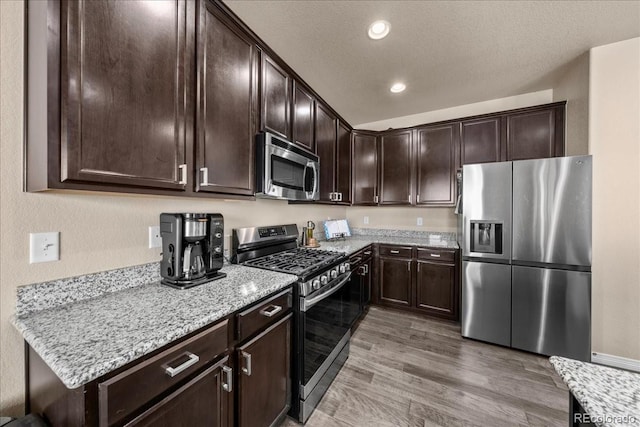 kitchen featuring dark brown cabinetry, wood finished floors, light stone counters, stainless steel appliances, and recessed lighting