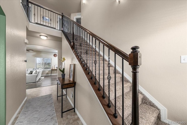 staircase featuring baseboards, arched walkways, and a high ceiling