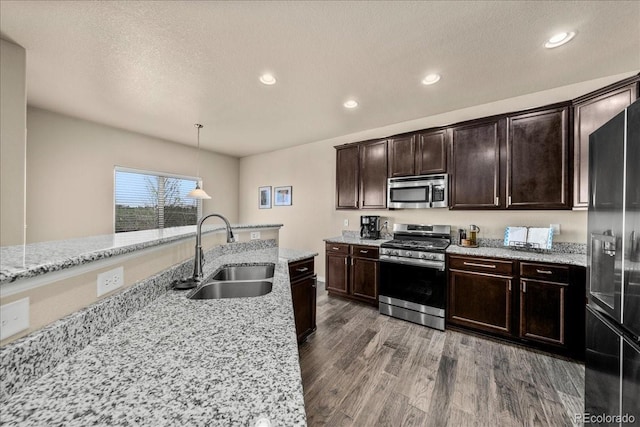 kitchen featuring dark brown cabinetry, wood finished floors, a sink, light stone counters, and stainless steel appliances