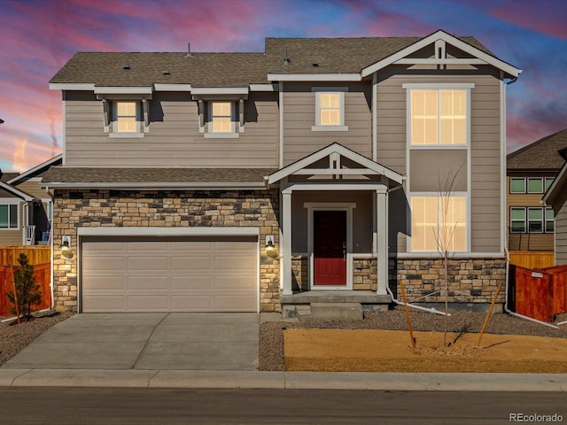 view of front facade with driveway, a shingled roof, stone siding, an attached garage, and fence