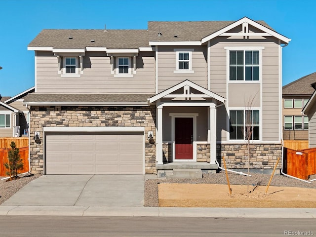 view of front of house with stone siding, concrete driveway, fence, a shingled roof, and a garage