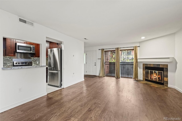 unfurnished living room with wood finished floors, a tiled fireplace, baseboards, and recessed lighting