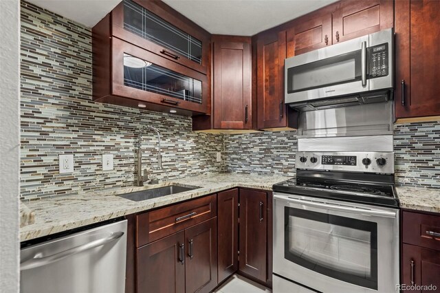 kitchen with stainless steel appliances, a sink, tasteful backsplash, and light stone counters