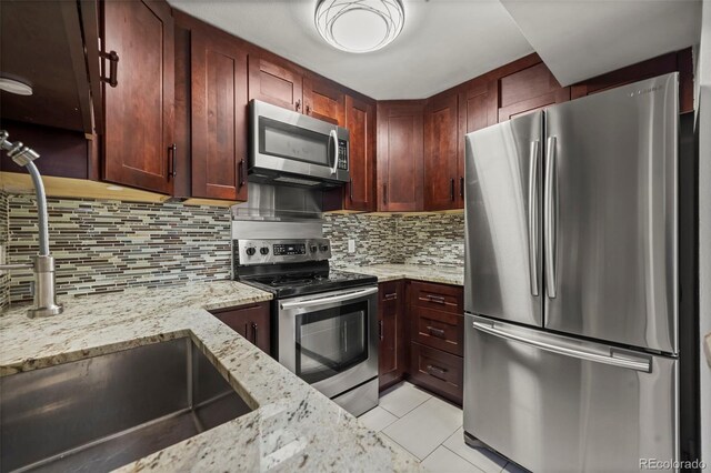 kitchen with stainless steel appliances, a sink, light tile patterned floors, backsplash, and light stone counters