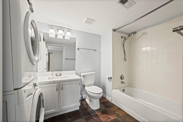 full bathroom featuring stacked washing machine and dryer, toilet, tub / shower combination, vanity, and stone finish flooring