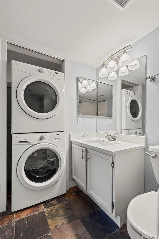 bathroom featuring stacked washer / drying machine, toilet, stone tile flooring, and vanity