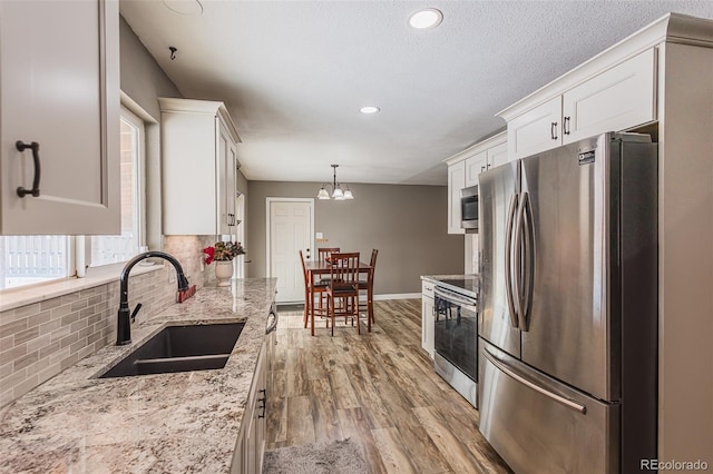 kitchen featuring white cabinetry, sink, backsplash, decorative light fixtures, and appliances with stainless steel finishes