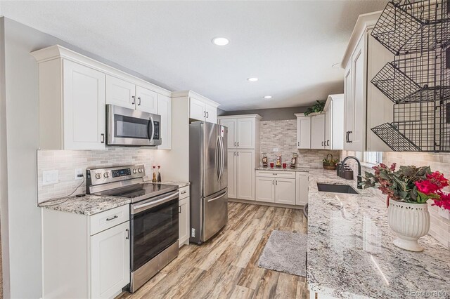 kitchen featuring white cabinets, sink, light stone countertops, appliances with stainless steel finishes, and light hardwood / wood-style floors