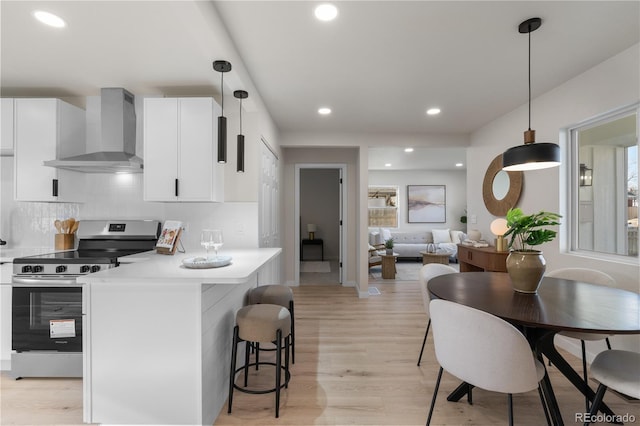 kitchen with wall chimney range hood, recessed lighting, a kitchen bar, stainless steel electric stove, and light wood finished floors