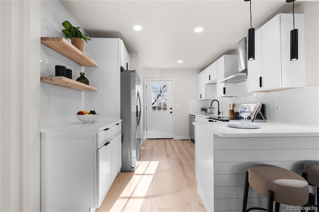 kitchen featuring light wood-type flooring, light countertops, open shelves, wall chimney exhaust hood, and stainless steel appliances