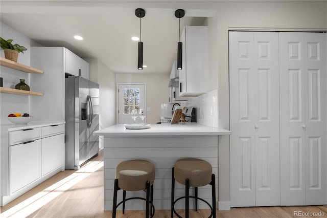 kitchen with stainless steel fridge with ice dispenser, light wood-style flooring, white cabinets, light countertops, and a breakfast bar area