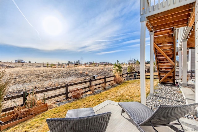 view of patio featuring a rural view, stairway, and fence