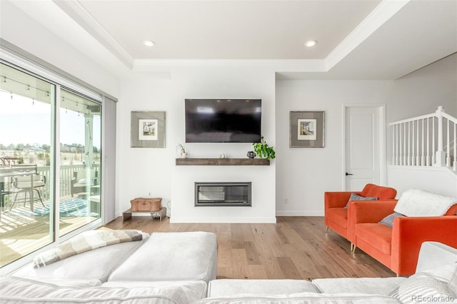 living room featuring a glass covered fireplace, a raised ceiling, wood finished floors, and recessed lighting