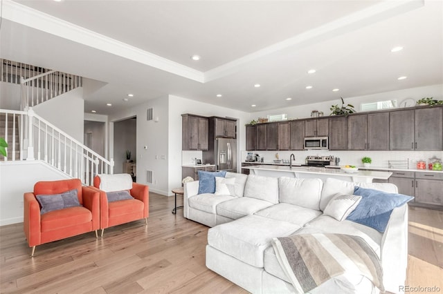 living room with light wood finished floors, baseboards, stairway, a tray ceiling, and recessed lighting