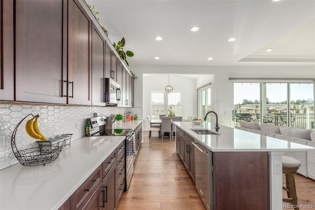 kitchen featuring a sink, tasteful backsplash, appliances with stainless steel finishes, a breakfast bar area, and light wood finished floors