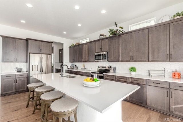 kitchen with a sink, a kitchen breakfast bar, light wood-style floors, and appliances with stainless steel finishes