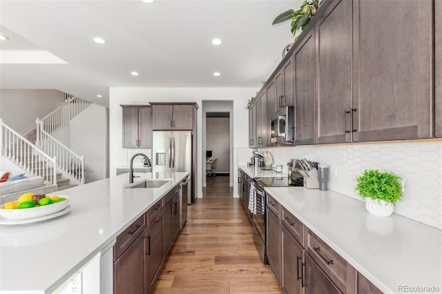 kitchen featuring a sink, backsplash, light wood-style floors, appliances with stainless steel finishes, and light countertops