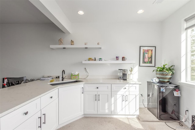 kitchen with a wealth of natural light, open shelves, light stone counters, and a sink