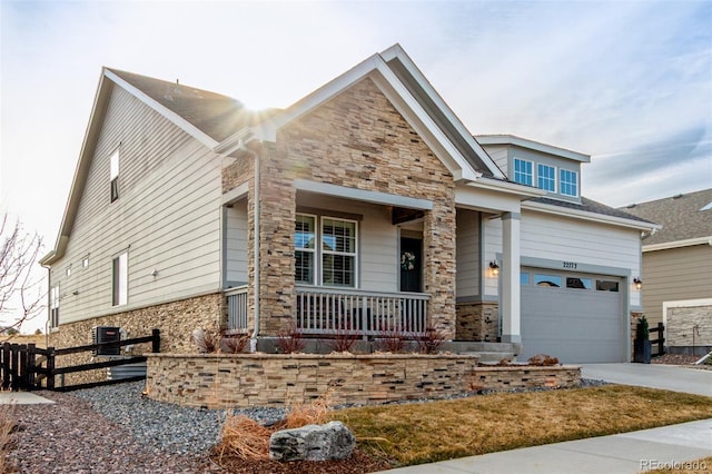 craftsman-style house featuring stone siding, covered porch, driveway, and fence