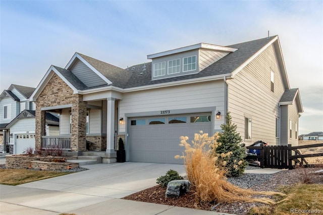 craftsman-style house with fence, driveway, a porch, a garage, and stone siding