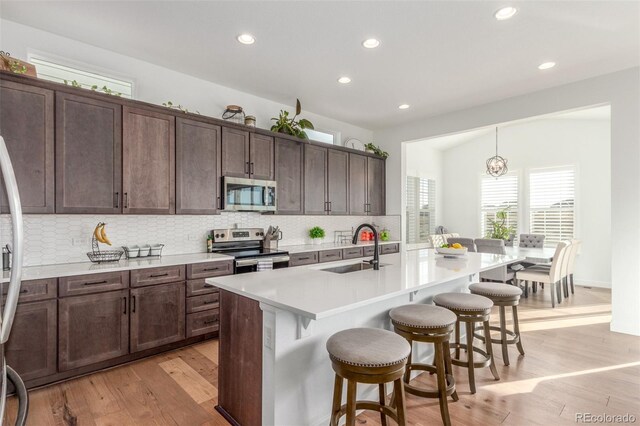 22773 E Narrowleaf Cir, Aurora, CO 80016 - kitchen featuring stainless steel appliances, a sink, light wood finished floors, a kitchen breakfast bar, and backsplash