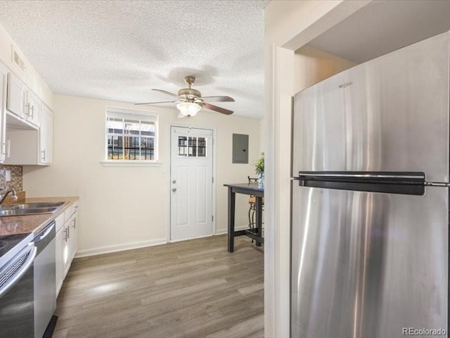 kitchen with light hardwood / wood-style floors, stainless steel appliances, sink, electric panel, and white cabinetry