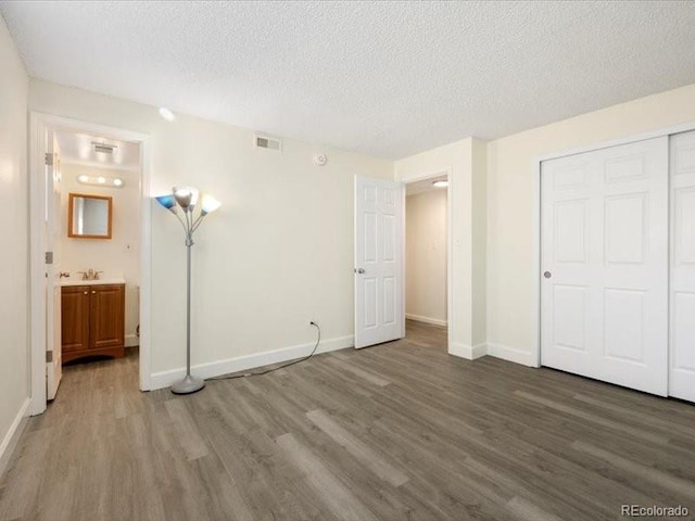 unfurnished bedroom featuring ensuite bathroom, a closet, dark wood-type flooring, and a textured ceiling