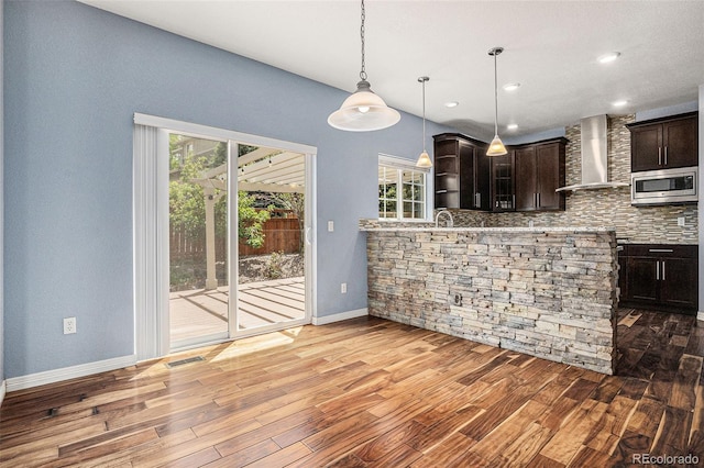 3389 Willowrun Dr, Castle Rock, CO 80109 - kitchen featuring wall chimney exhaust hood, stainless steel microwave, baseboards, dark brown cabinetry, and wood finished floors