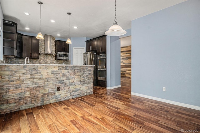 3389 Willowrun Dr, Castle Rock, CO 80109 - kitchen featuring wall chimney range hood, backsplash, appliances with stainless steel finishes, wood finished floors, and dark brown cabinetry