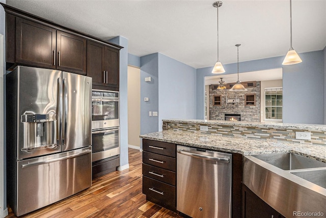 3389 Willowrun Dr, Castle Rock, CO 80109 - kitchen with stainless steel appliances, wood finished floors, dark brown cabinets, decorative backsplash, and light stone countertops