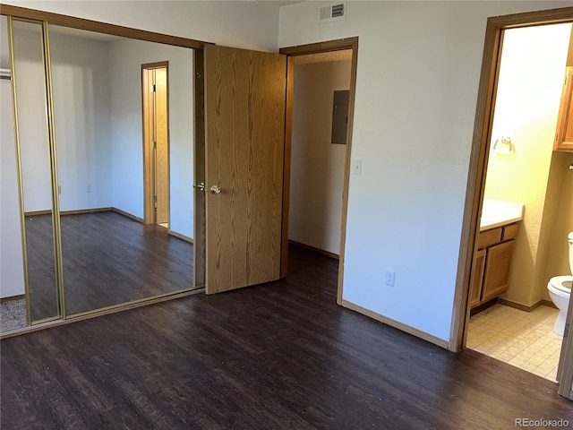 unfurnished bedroom with connected bathroom, a closet, dark hardwood / wood-style flooring, and electric panel