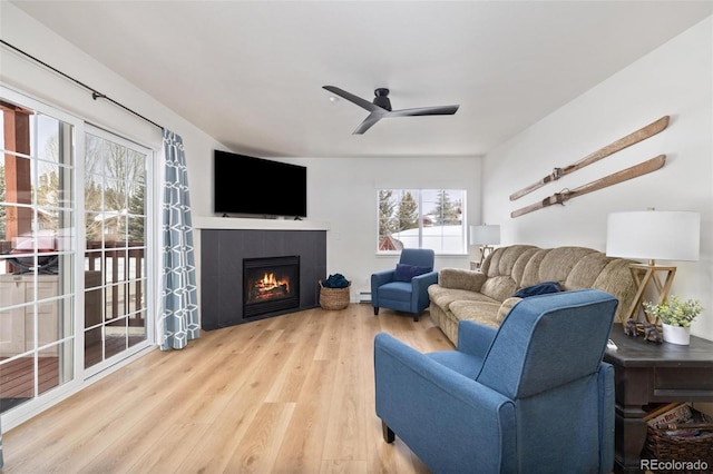 living room with a baseboard radiator, a tiled fireplace, wood finished floors, and a ceiling fan