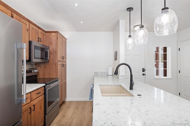 kitchen featuring light wood finished floors, decorative backsplash, light stone counters, stainless steel appliances, and a sink