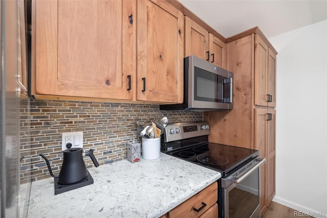 kitchen featuring stainless steel appliances, baseboards, light stone counters, and decorative backsplash