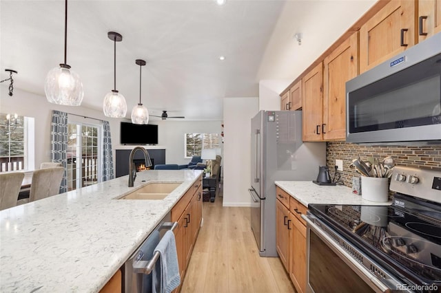 kitchen featuring light wood finished floors, backsplash, appliances with stainless steel finishes, a sink, and a lit fireplace