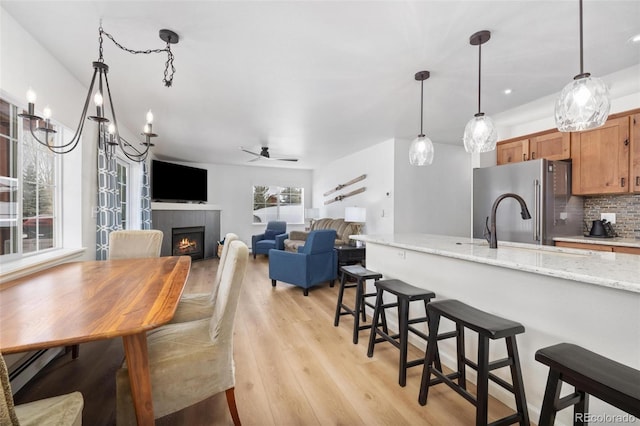 kitchen with backsplash, freestanding refrigerator, light wood finished floors, brown cabinetry, and a tiled fireplace