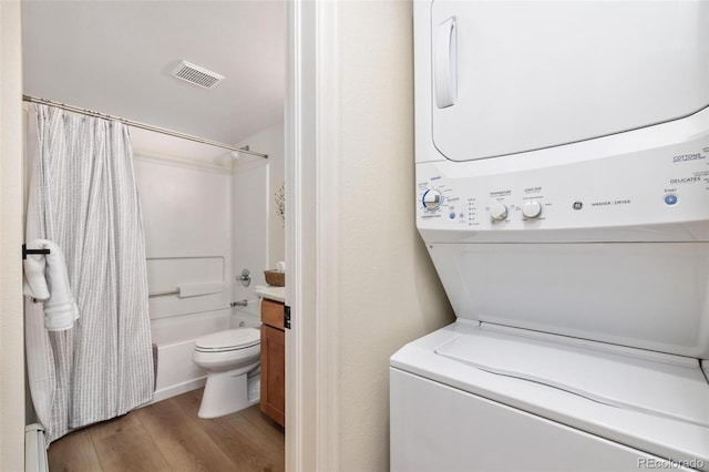 laundry room with laundry area, visible vents, stacked washer / dryer, and wood finished floors