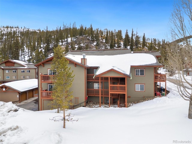 snow covered back of property with a chimney and a wooden deck