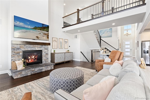 living room with a stone fireplace, visible vents, wood finished floors, and baseboards