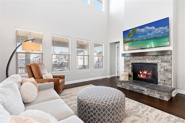 living area with a stone fireplace, a towering ceiling, baseboards, and wood finished floors