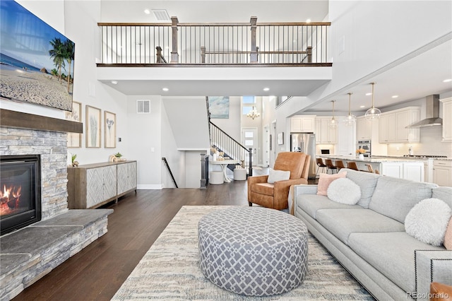 living room featuring visible vents, a stone fireplace, dark wood finished floors, and a towering ceiling