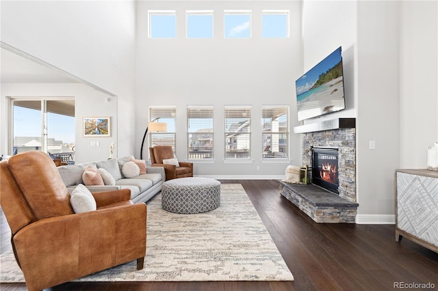 living room featuring dark wood finished floors, a stone fireplace, baseboards, and a towering ceiling