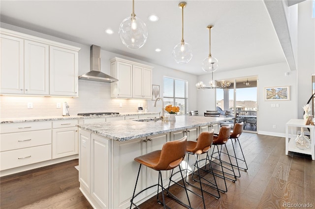 kitchen featuring dark wood finished floors, decorative backsplash, stainless steel gas stovetop, white cabinetry, and wall chimney range hood